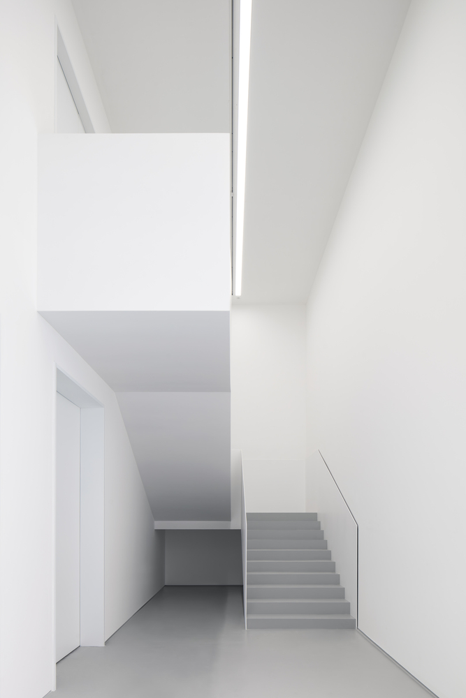 Stairwell: white walls, grey stairs with glass balustrade, double-height void, linear skylight above