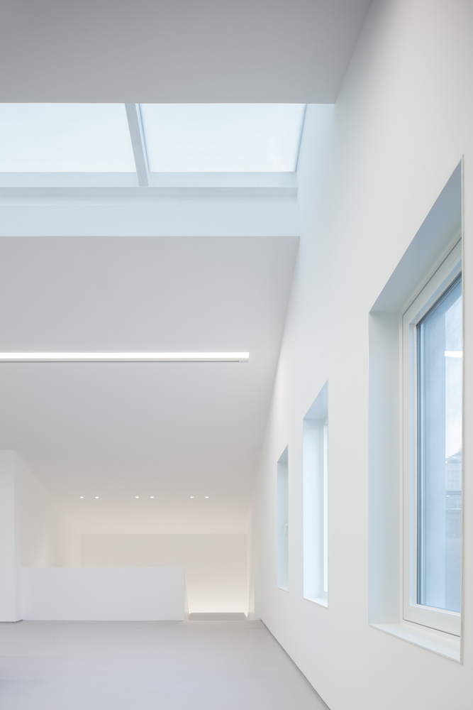 Second-floor gallery: skylight above, double-height window wall to the street, white walls, recessed ceiling lights below