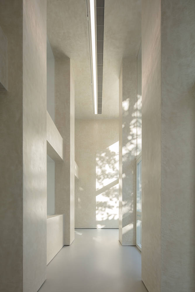 Facade at night: warm light flooding through the three glass openings, white concrete glowing, columns casting shadows
