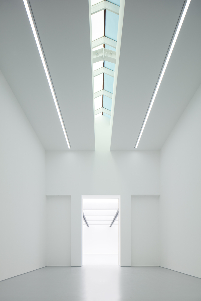Lobby perspective: skylight strip above, white walls converging toward a bright opening, grey polished floor