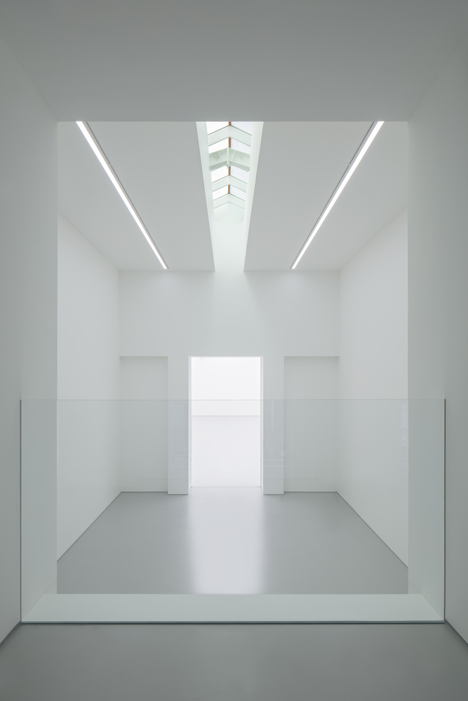 Second-floor void from above: glass balustrade at the edge, white walls, skylight converging above, gallery below