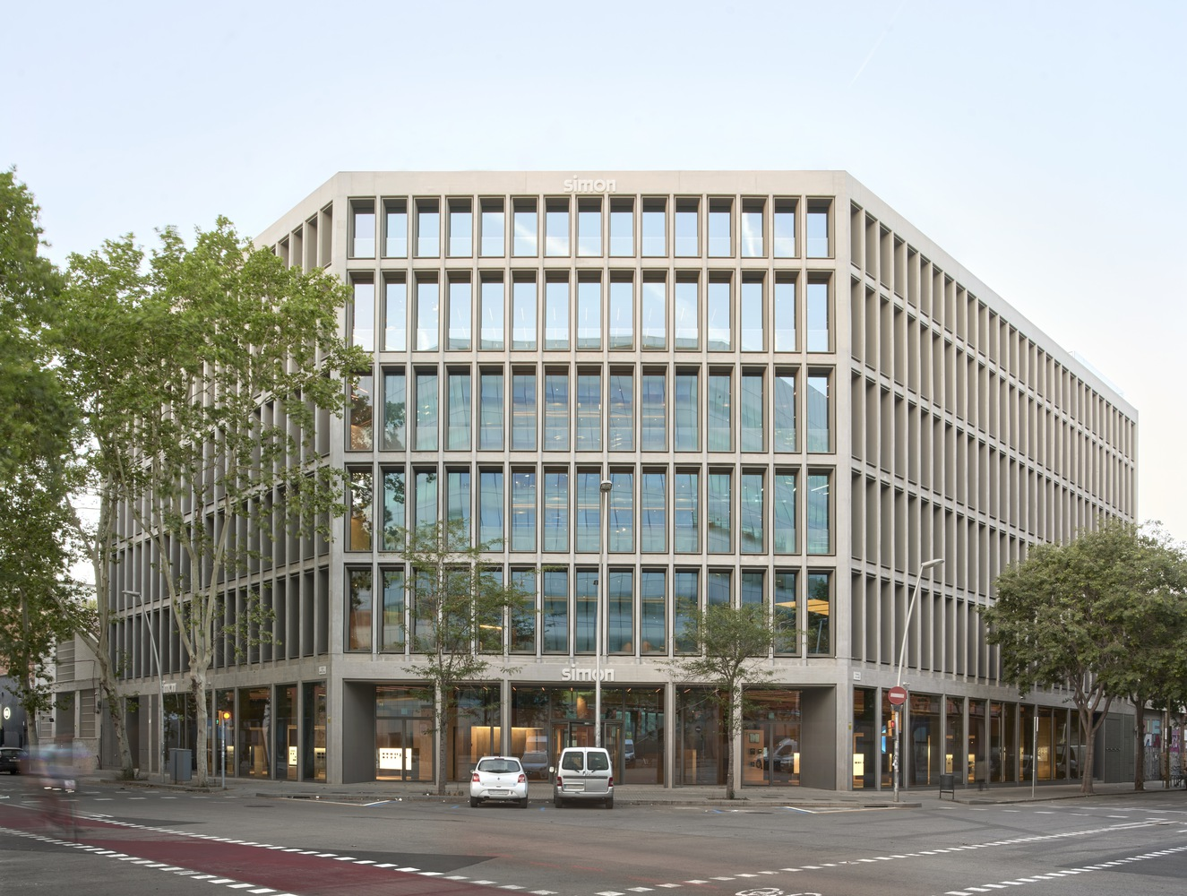 Street corner: the rehabilitated building with vertical concrete fins, full-height glazing, mature trees, bike lane