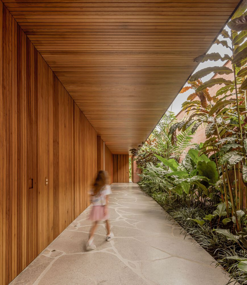 Covered walkway with slatted timber ceiling and wall alongside planted bed with tropical foliage