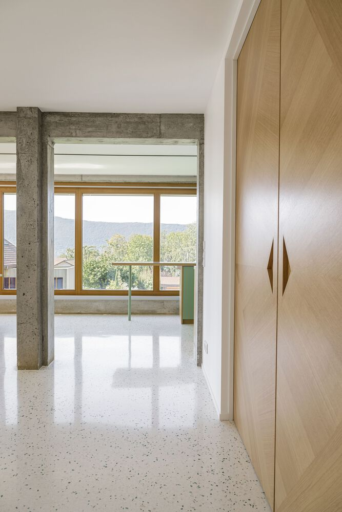 Corridor: timber wardrobe, concrete beam overhead, terrazzo floor, green kitchen glimpsed through the opening