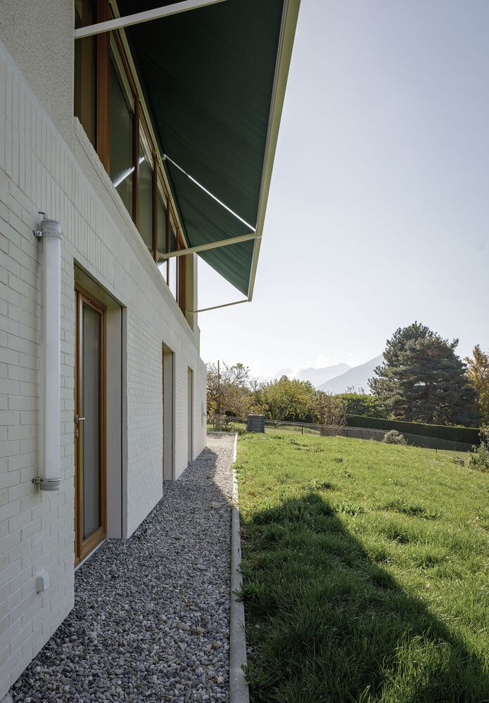 Side passage: green awning overhead, gravel path along white rendered wall, garden beyond