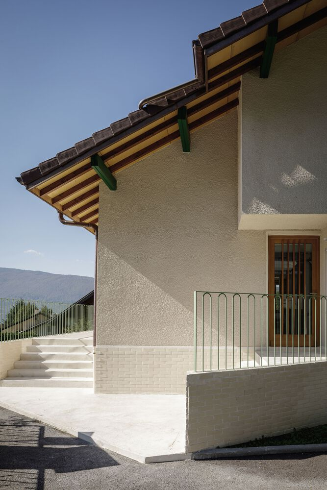 Entry side: concrete stair, timber door, exposed rafters, balcony railing shadow
