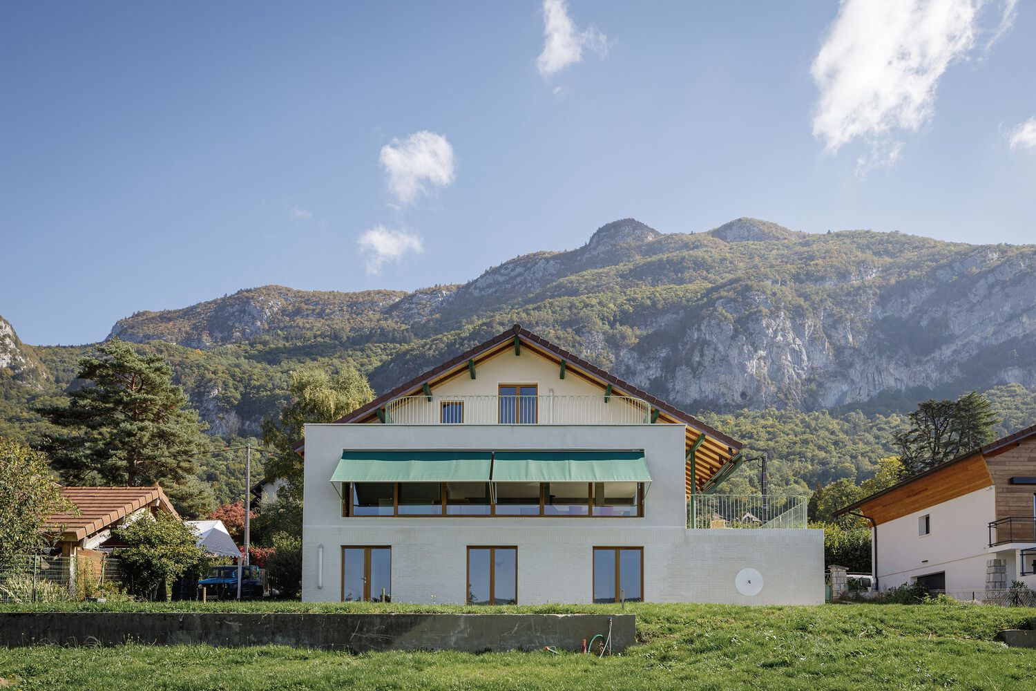 Full garden view: the complete villa with mountains behind, green awning, white brick base, lawn