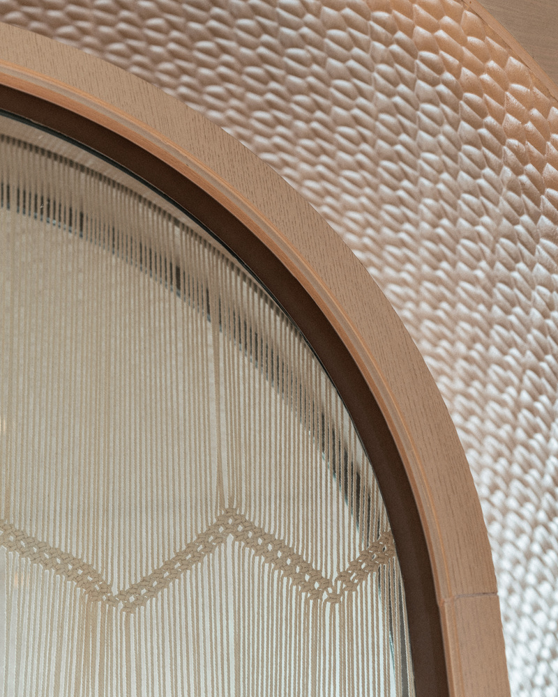 Ceiling detail: woven rattan panel inside an arched timber frame, fringe curtain behind