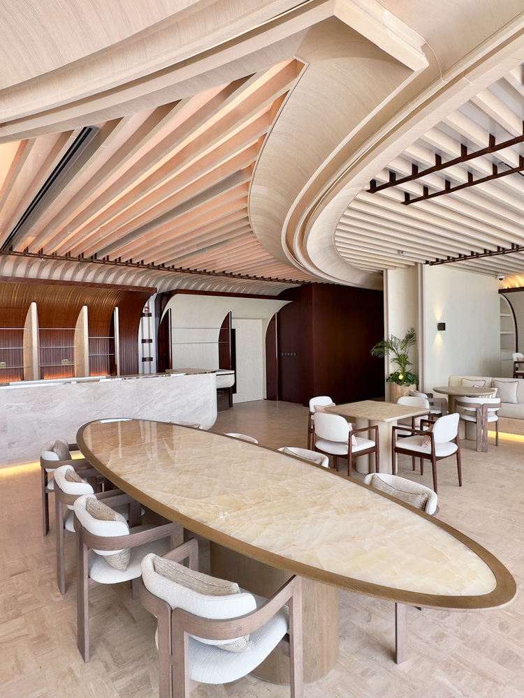 Ilios dining: curved timber ceiling sweeping over an oval table, white upholstered chairs