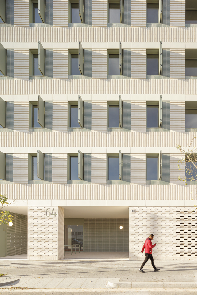 Entry detail: perforated ceramic screen at ground level, number 64 above the entrance, figure walking past, balconies above