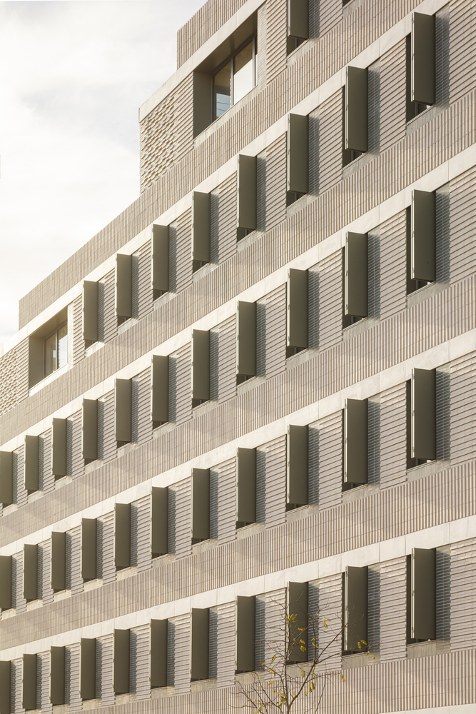 Facade rhythm: angled metal shutters in varying positions, cream brick piers, horizontal bands, viewed from below