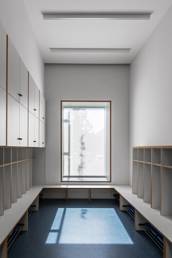 Changing room: grey lockers with timber cubbies, bench seating, blue floor, window to the garden