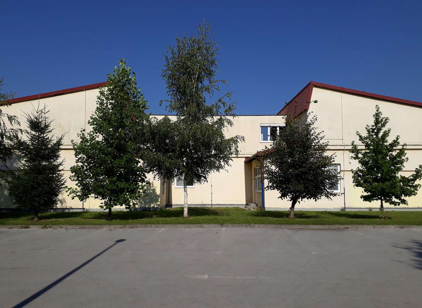Before: the original school building, plain rendered walls, red metal roof, mature trees, no extension