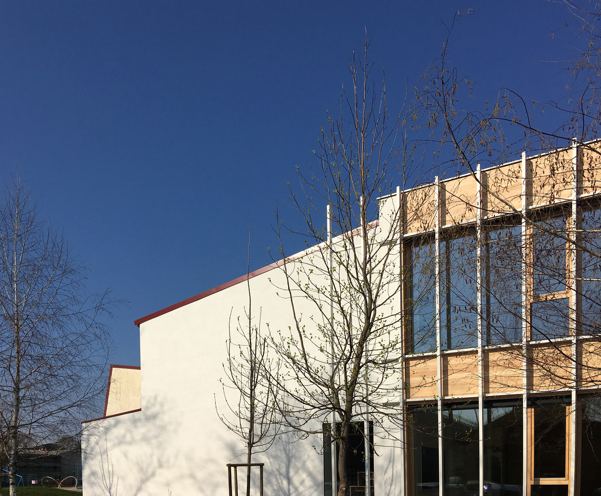 Upper corner: timber-clad classroom volume above the white rendered ground floor, winter light