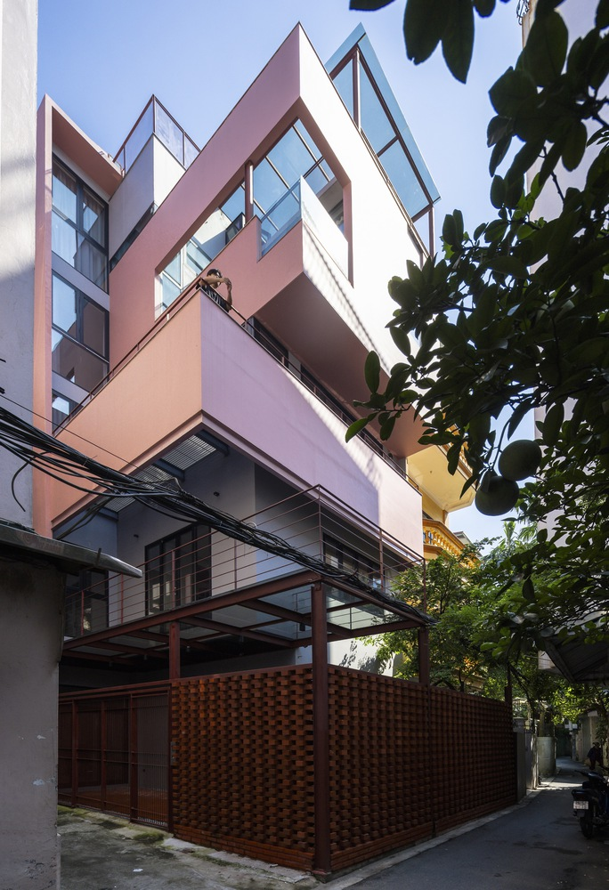 Street view of the angular facade with perforated brick enclosure and steel canopy beneath overhanging tree branches