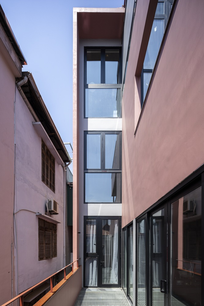 Narrow courtyard framed by pink stucco walls with a stacked glass volume rising between them