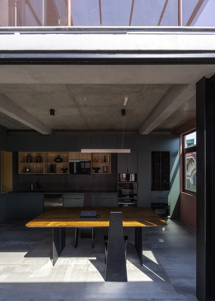 Kitchen and dining area with exposed concrete ceiling and sunlight streaming across timber table