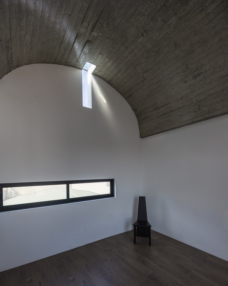 Vaulted ceiling room with board-formed concrete and a narrow skylight casting daylight down white walls