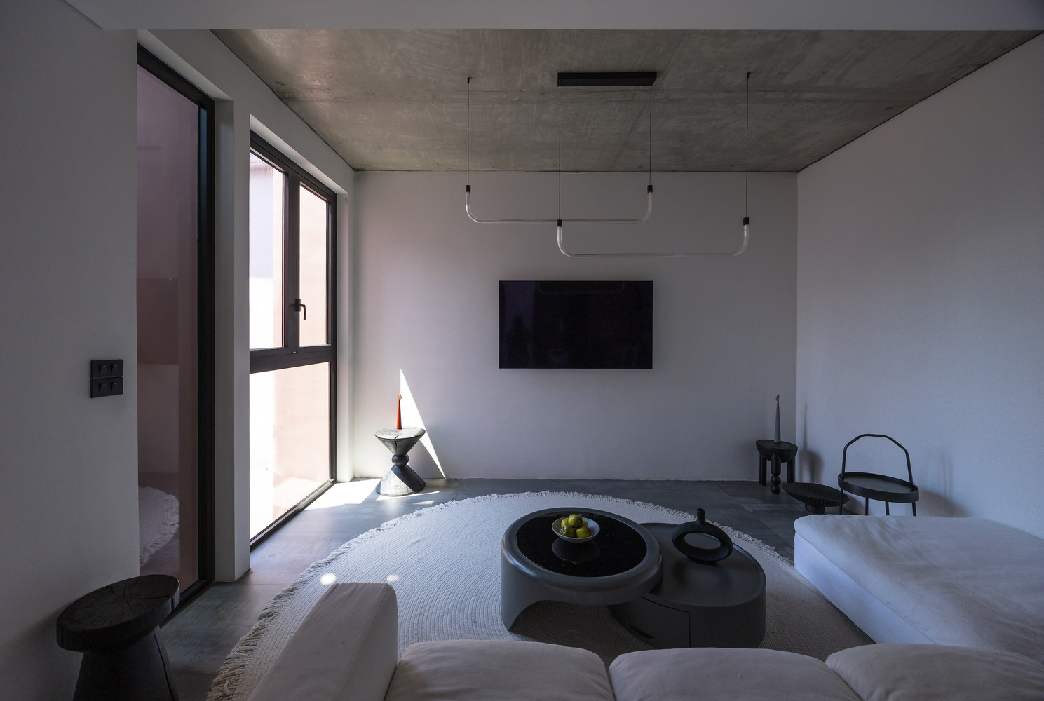 Living area with sunken circular seating and concrete ceiling lit by afternoon sun through tall windows