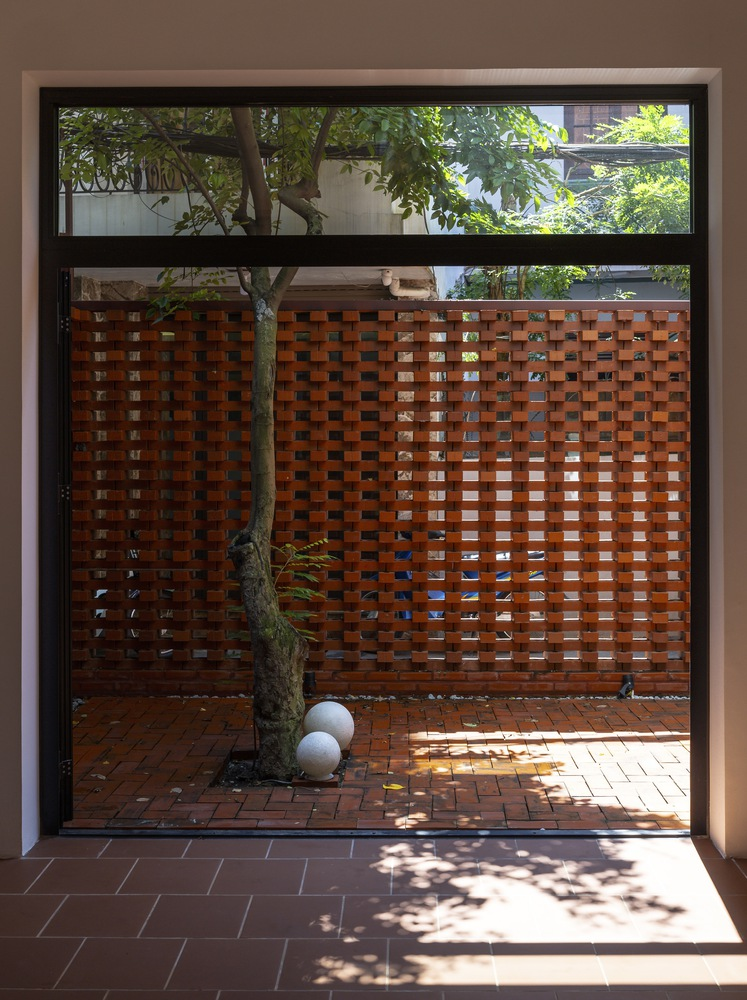 View through doorway to brick courtyard with young tree and perforated screen wall in dappled sunlight