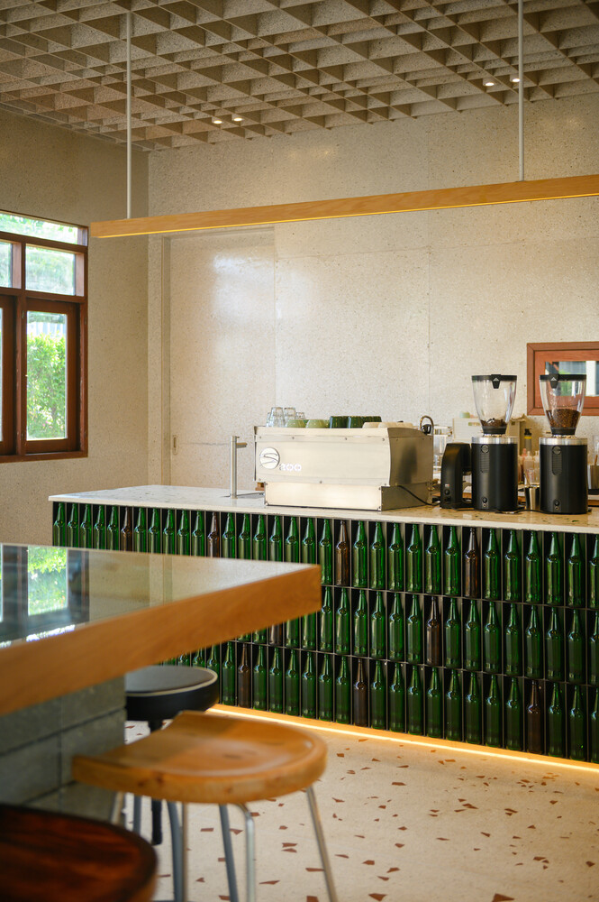 Counter detail: green glass bottles set vertically as bar front, terrazzo top, timber bar ledge