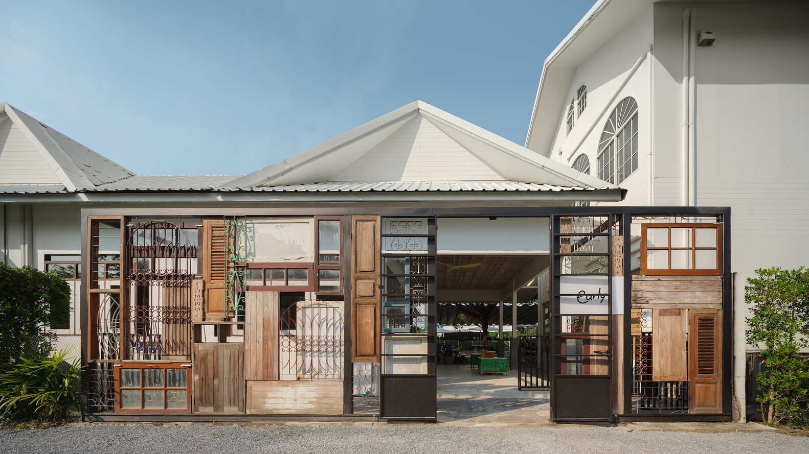 Street facade wider view: the full patchwork of reclaimed elements, white gable roof behind, Early signage