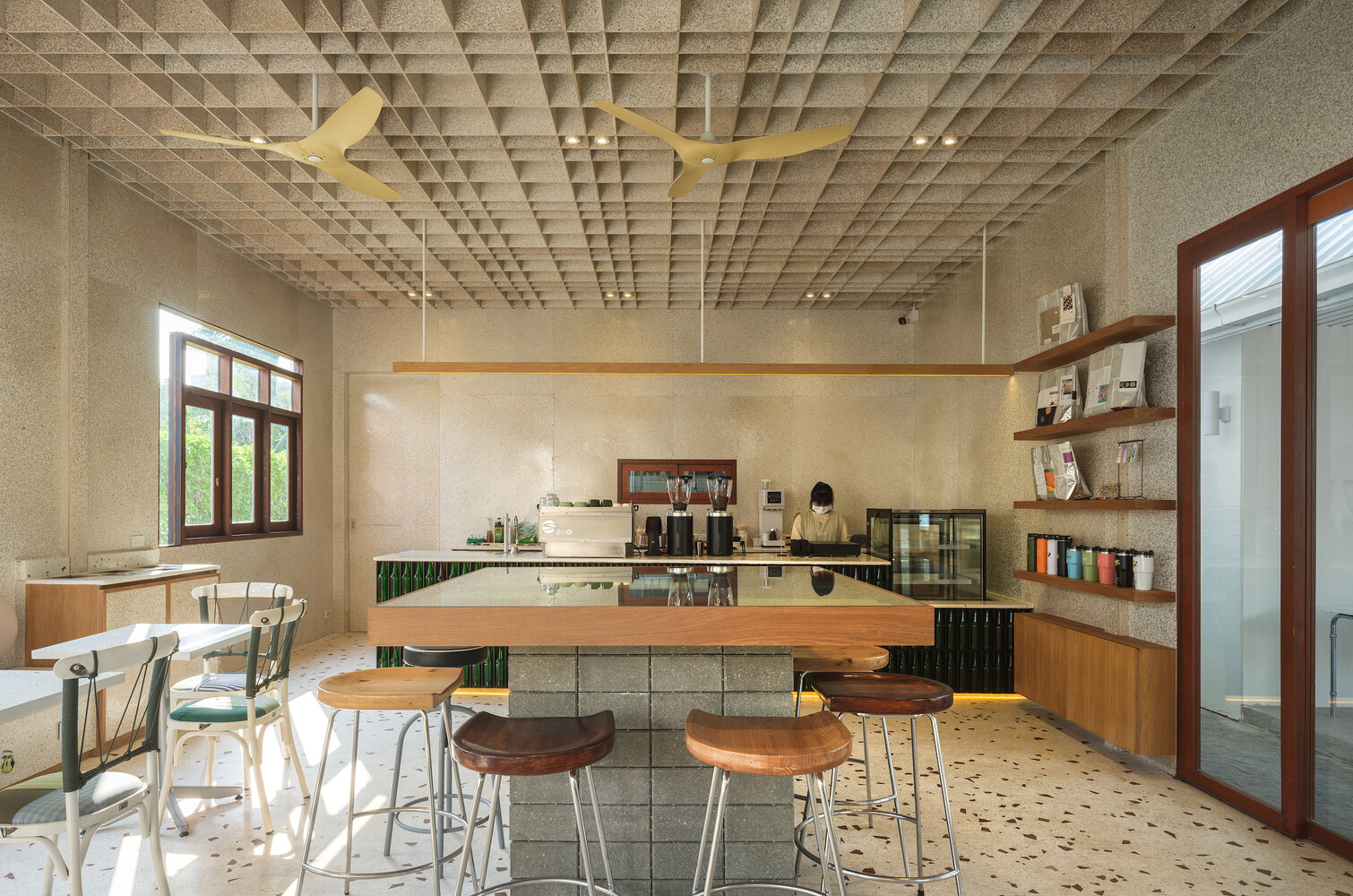 Full interior: waffle ceiling with fans, bar stools at counter, tables along window wall, terrazzo floor