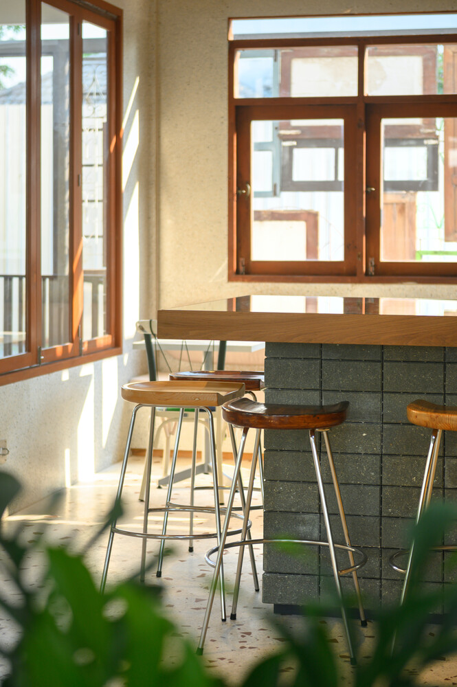 Window seating: high stools along a concrete-block counter beside salvaged timber-framed windows