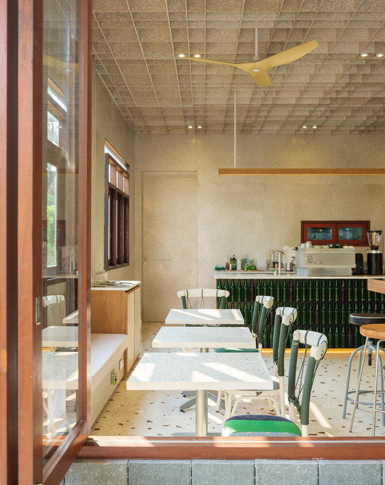 Interior through window: tables, green chair cushions, afternoon sun on the terrazzo floor