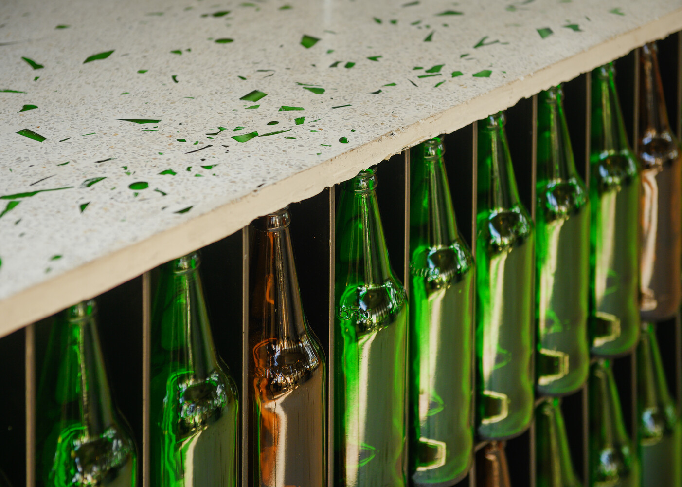 Close-up: inverted green and amber bottles beneath the terrazzo counter edge