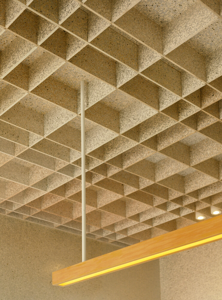 Ceiling detail: exposed waffle grid in recycled material with timber light bar and brass fan
