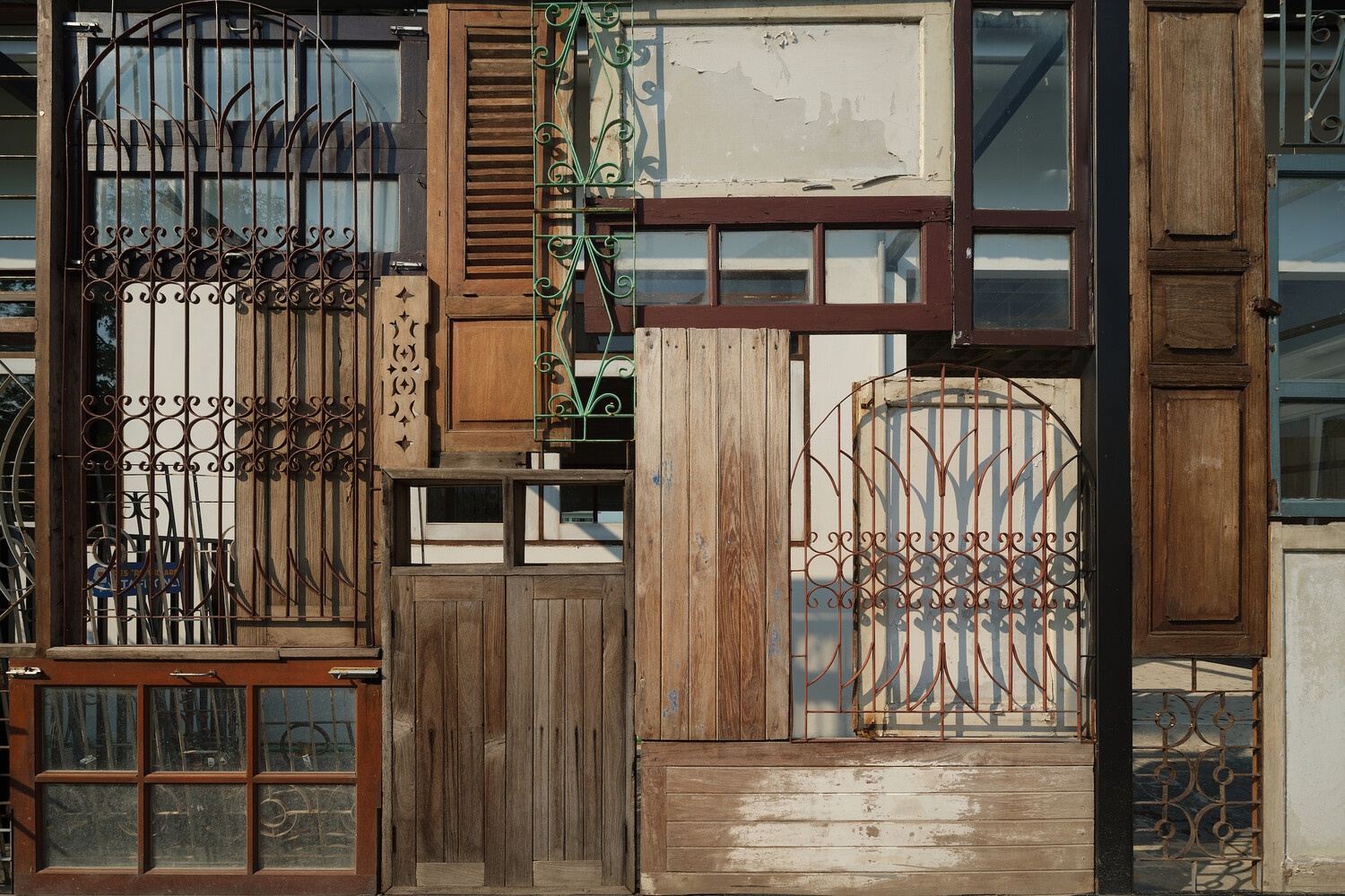 Facade close-up: the full collage of salvaged ironwork, timber shutters, louvres, and glass panels