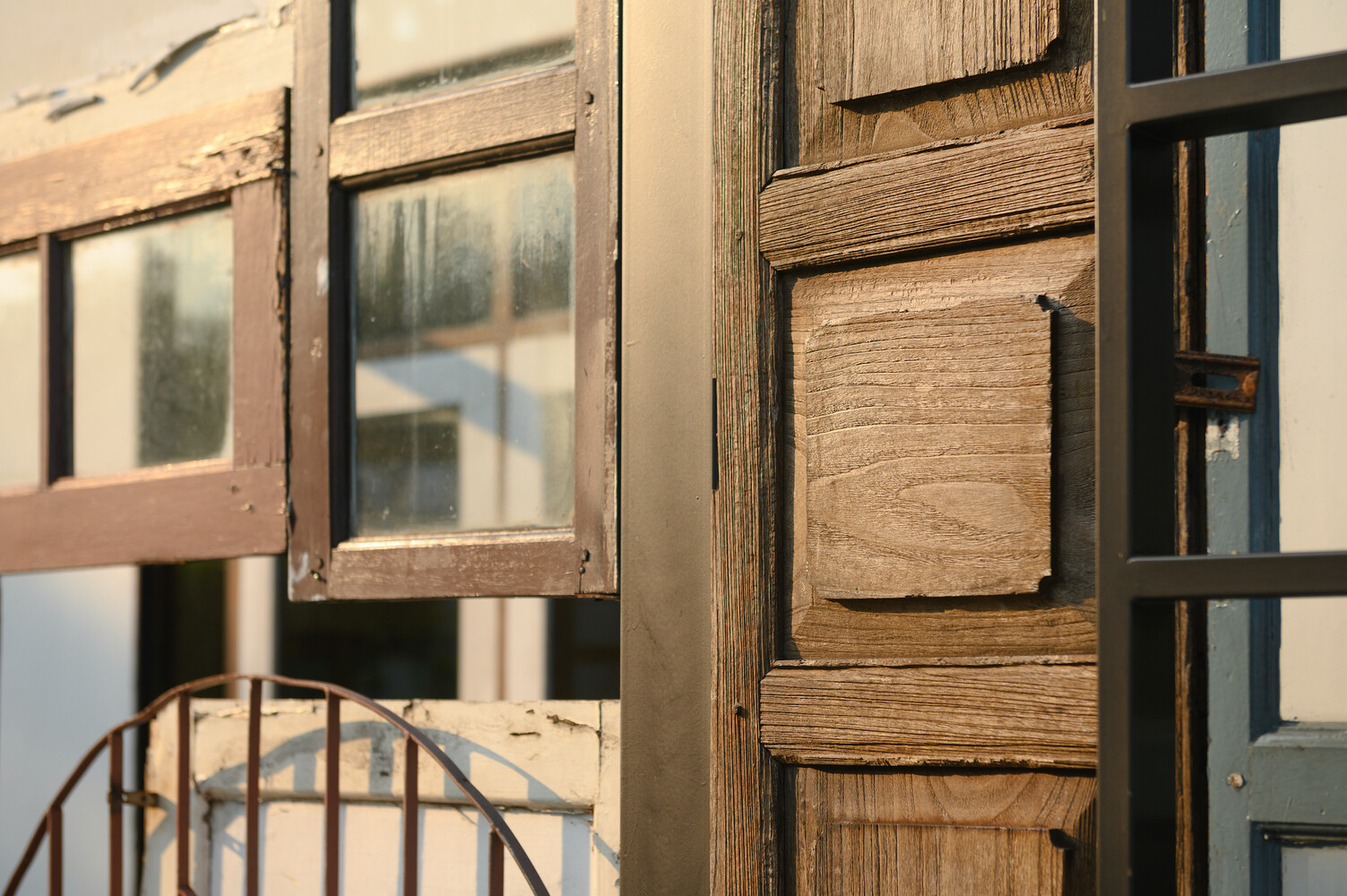 Facade detail: aged timber door panel and iron grille junction, showing patina and hardware