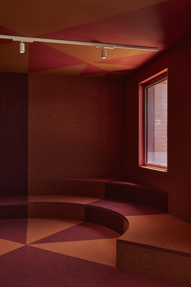 Interior room with curved seating platform in gradient red and orange tones under colored ceiling planes