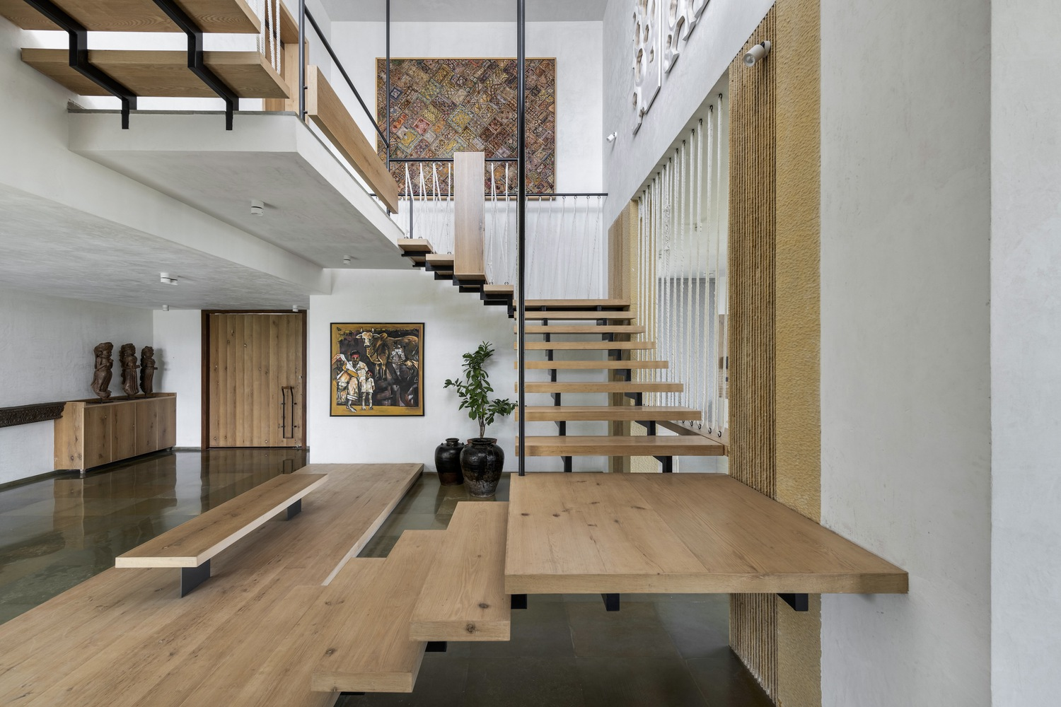 Entry hall: floating timber stair with steel stringer, double-height void, jute wall panel, art collection on display, polished stone floor