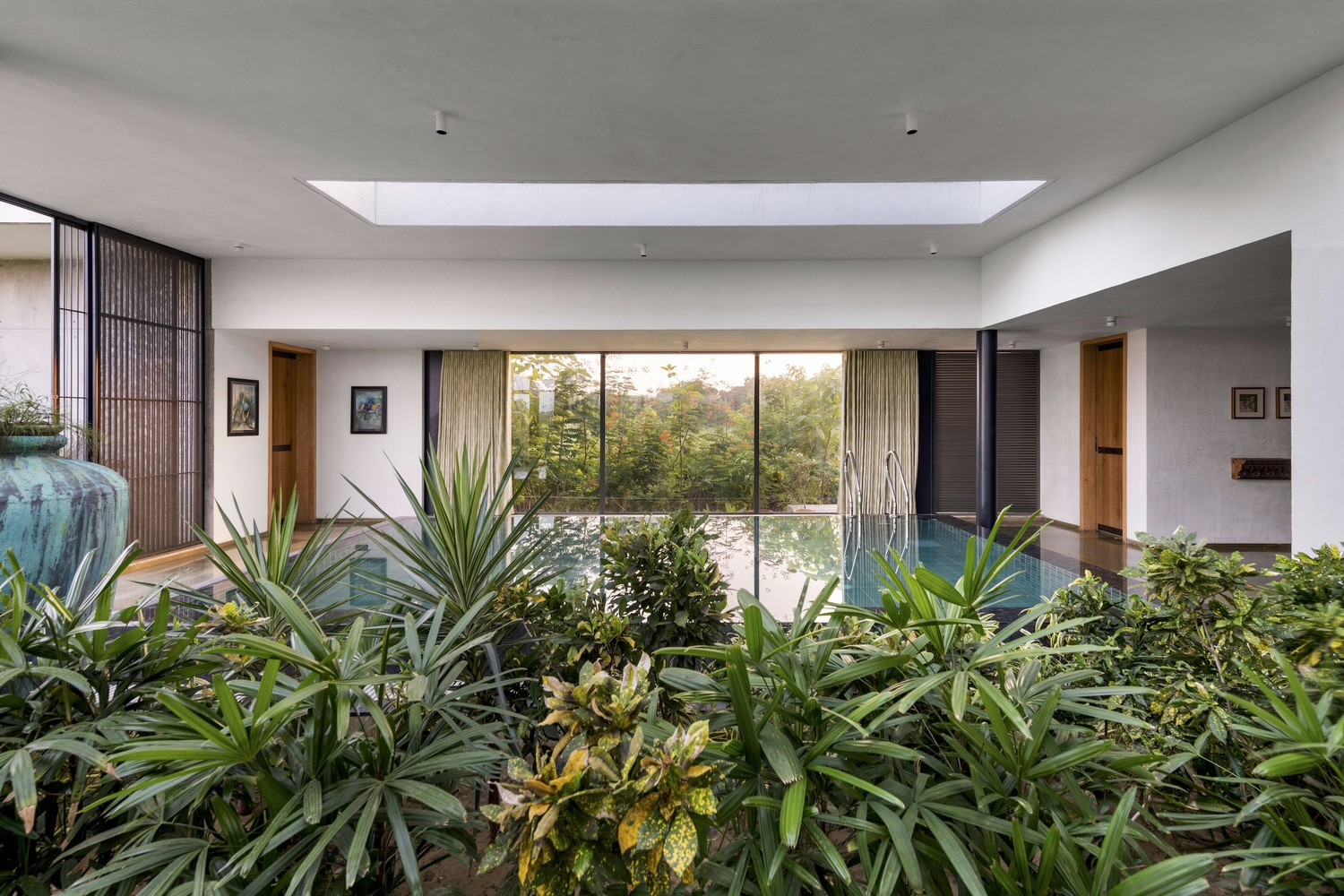 Internal courtyard: dense tropical planting under a large skylight, pool and curtained rooms visible through the glazing beyond