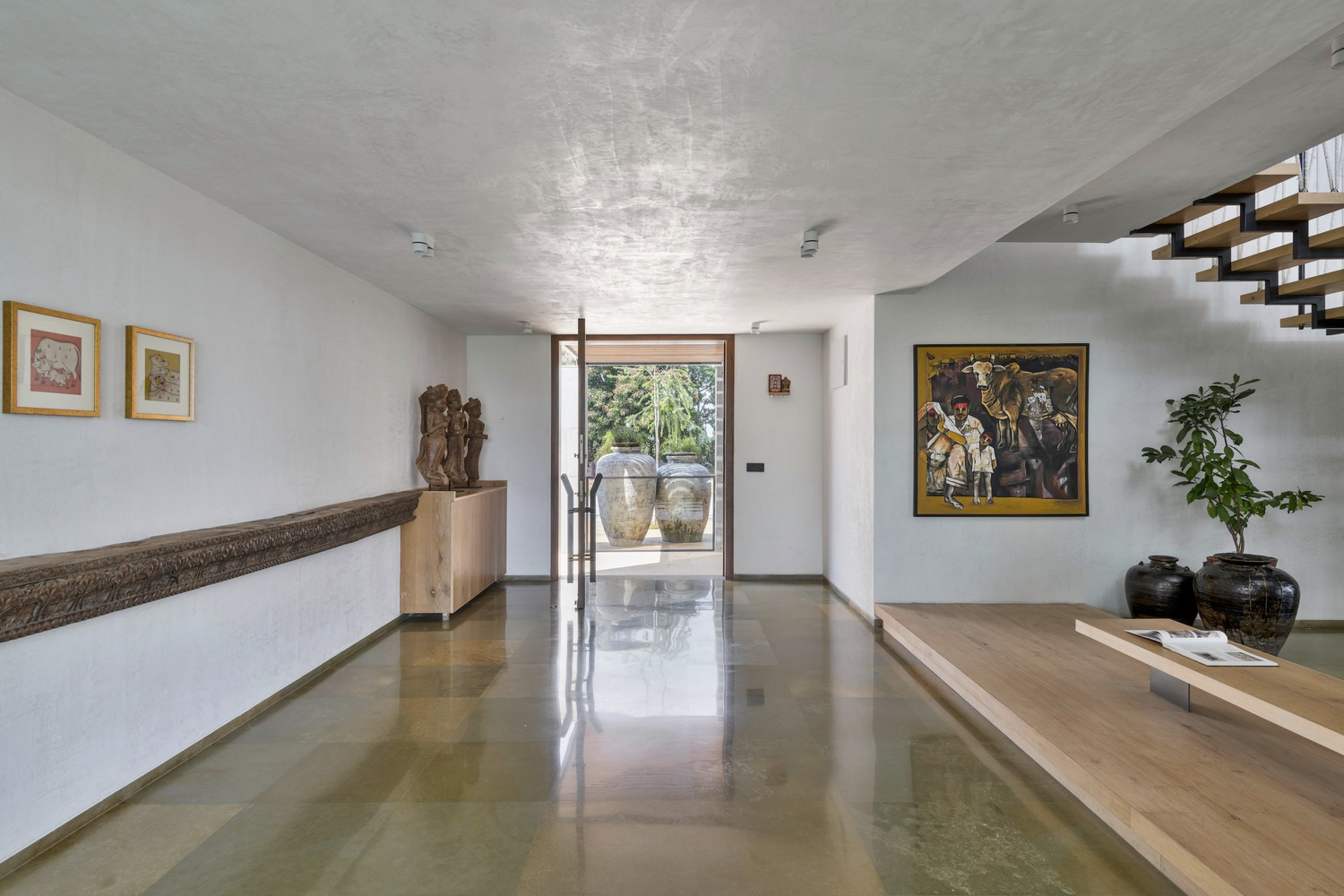 Gallery corridor: polished stone floor, art and sculpture on display, white walls, timber stair visible at the far end, exposed concrete ceiling
