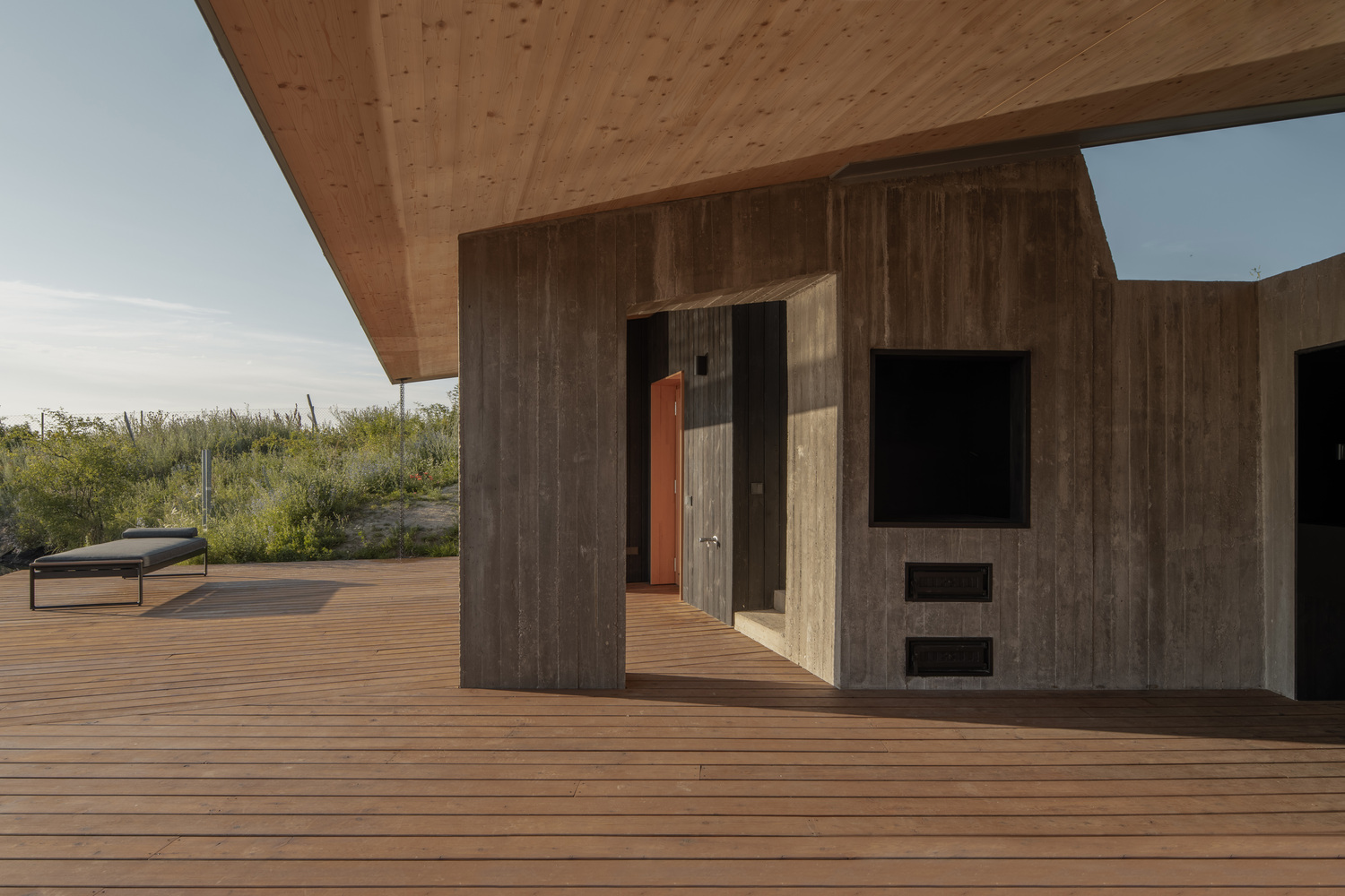 Deck detail: charred timber and concrete wall with built-in fireplace and TV recess, timber deck, meadow beyond
