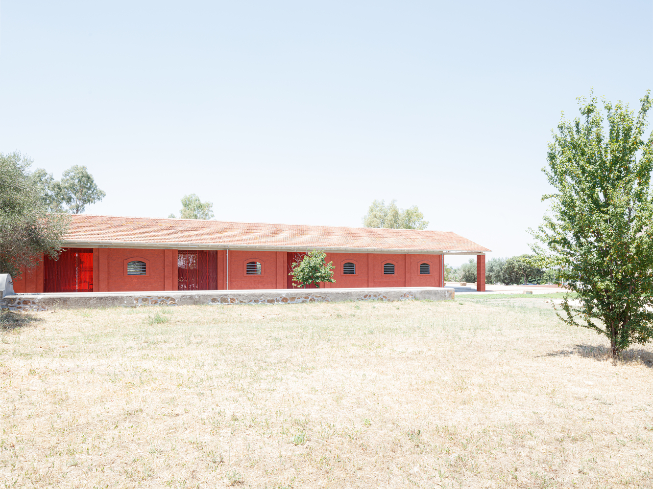 Red brick facade with tiled roof and louvered vents set in a dry summer landscape