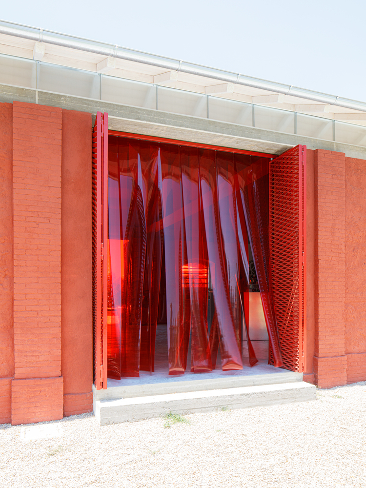 Entry threshold with red translucent strip curtains and textured brick jambs in daylight