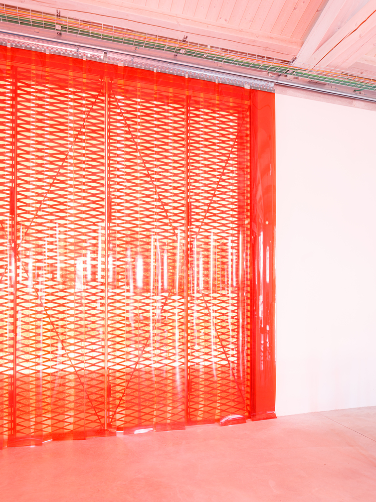 Red perforated metal screen partially opened to reveal an interior courtyard bathed in light