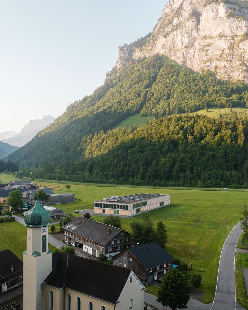 Aerial view of the long industrial shed with clerestory windows set in a valley below forested cliffs