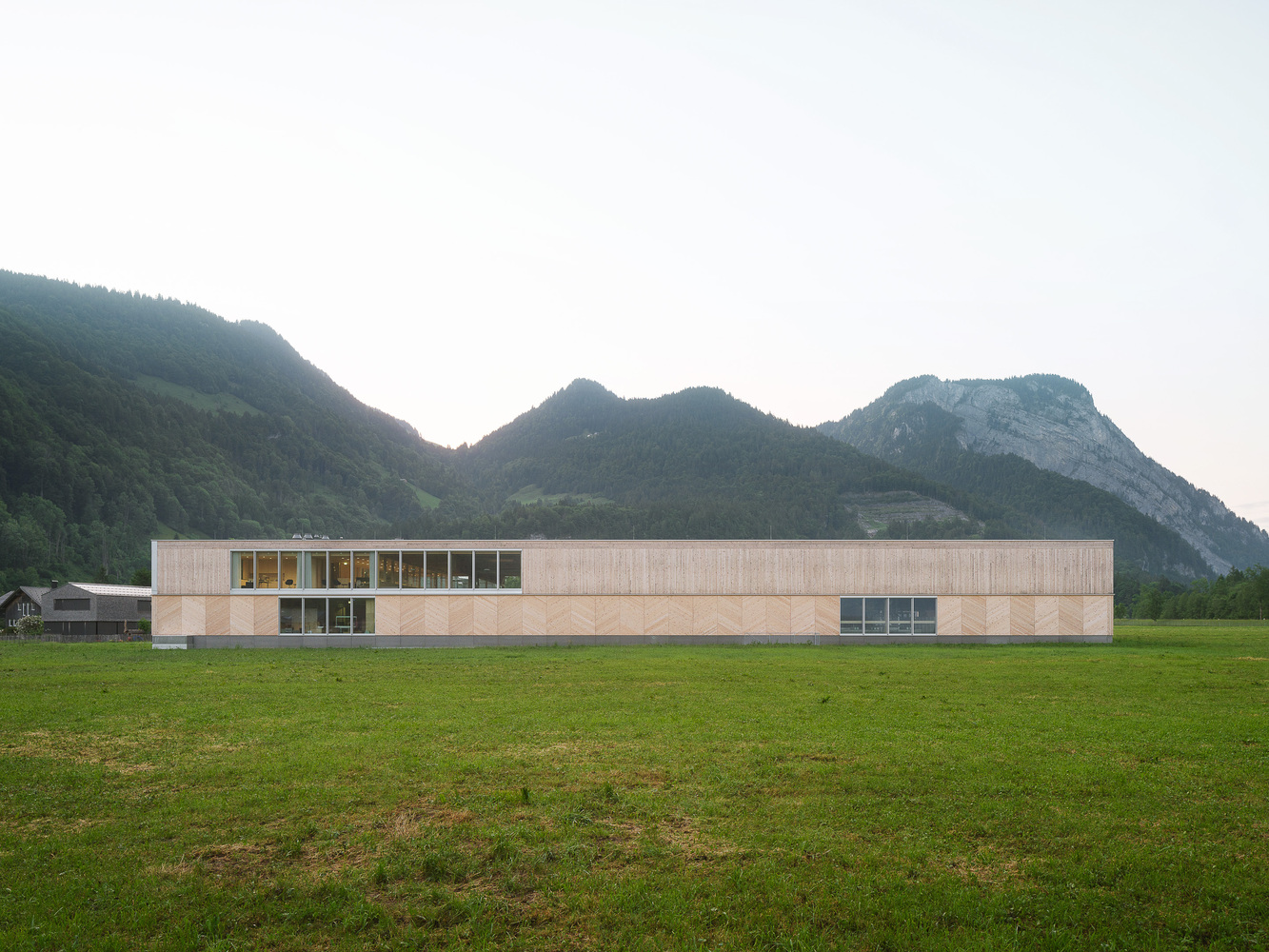 Linear facade with timber cladding and ribbons of glazing stretching across an open meadow at dusk