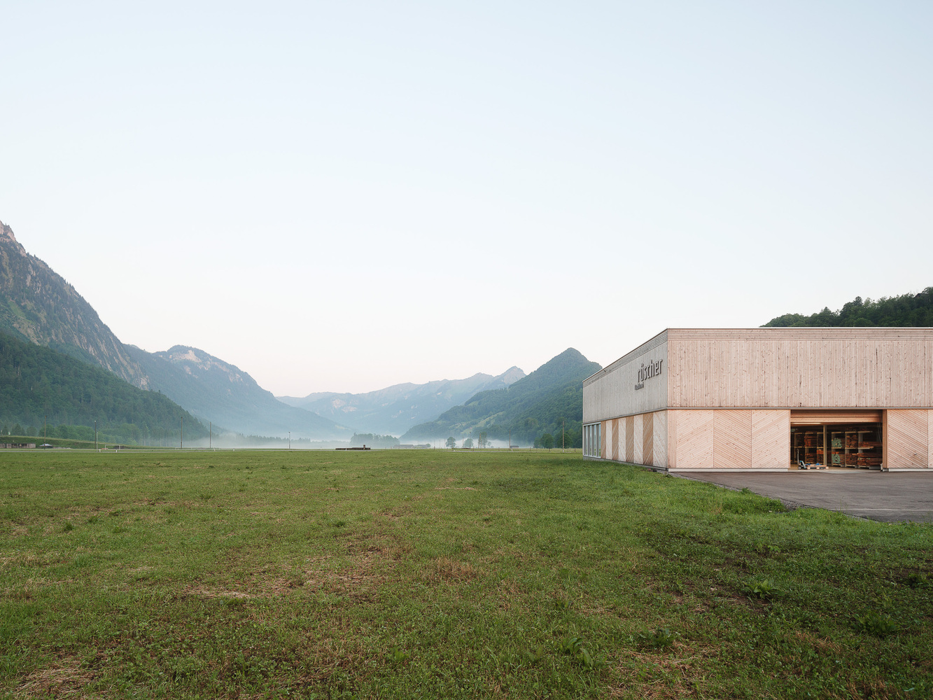 Corner of the timber-clad volume with entry canopy at dawn with mist hanging over distant mountains