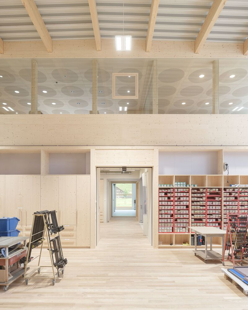 Two-story workspace with glass partitions and material storage shelving under cross-laminated timber beams
