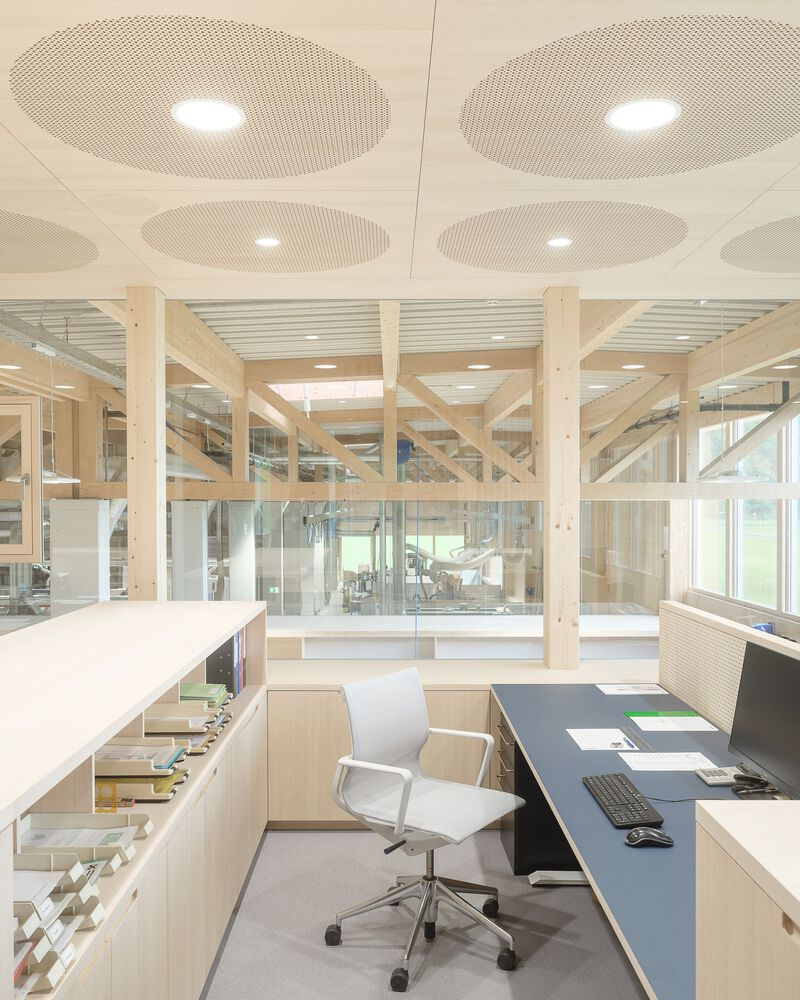 Office area with perforated circular ceiling panels and workstation beneath timber beam structure