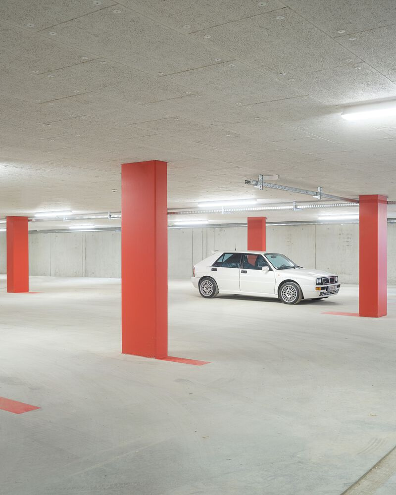 Underground parking garage with red square columns and a white car under fluorescent lighting