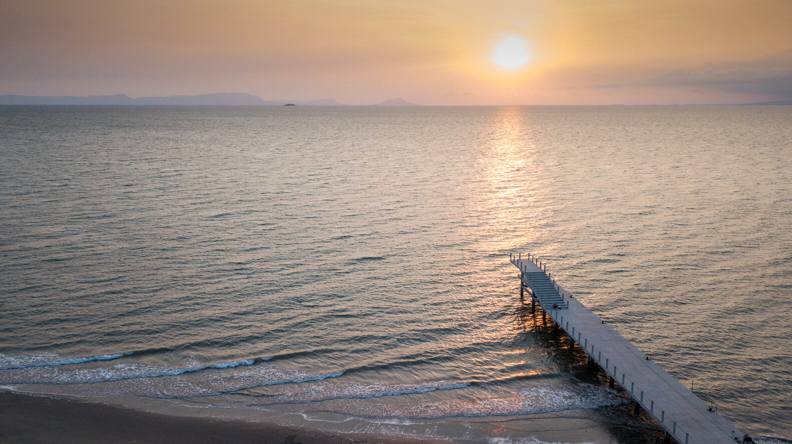 Aerial view of white concrete jetty stretching into calm water at golden hour