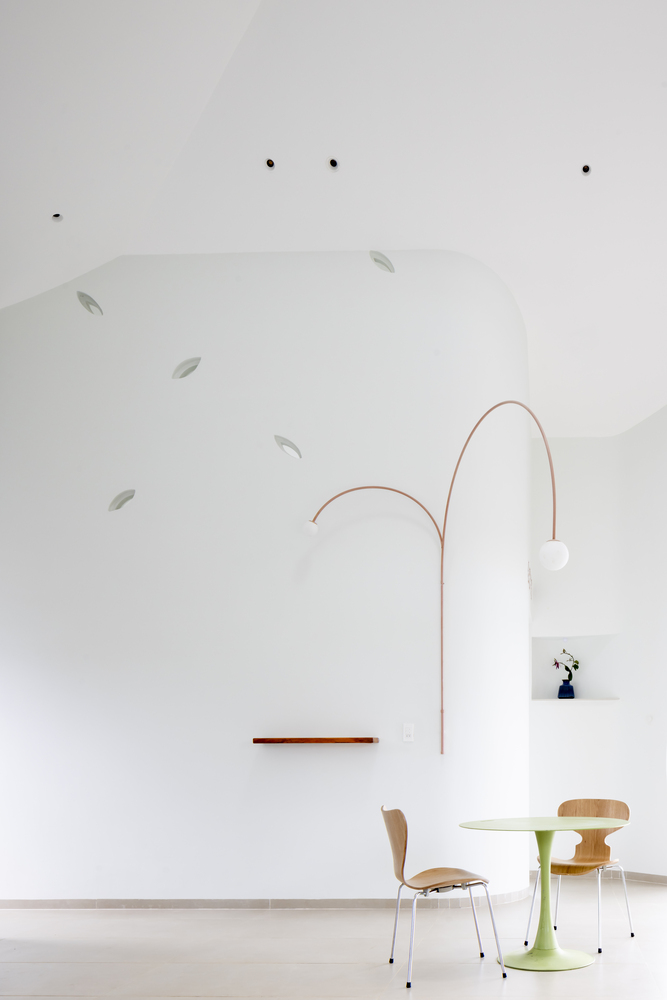 Dining area beneath curved ceiling plane with copper arc lamp suspended over plywood chairs and round table