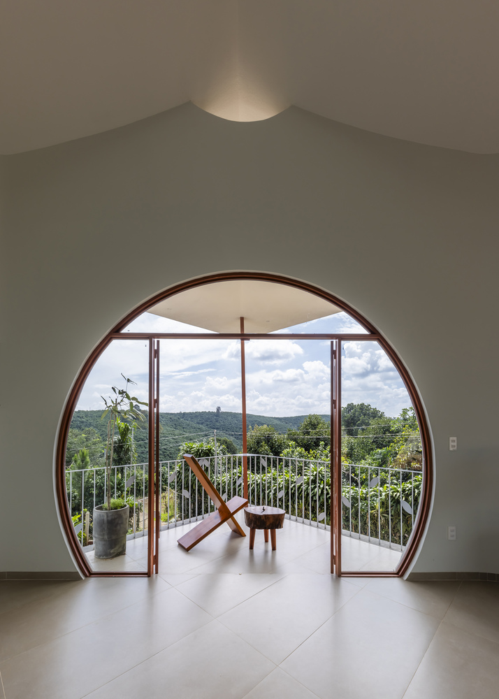 Circular door opening with timber frame leading to balcony with folding chair and view of forested hillside